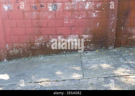 Weathered red brick wall with white spots on sidewalk Stock Photo