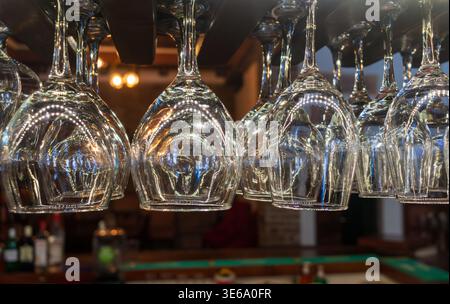 Upside-down wine glasses hanging at a cozy bar with bottles Stock Photo