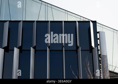 Contemporary office building exterior showcasing a dark facade with geometric vertical louvers and large glass panels reflecting light in a clean arch Stock Photo