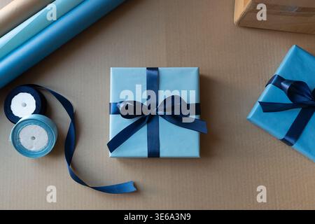 Wrapped gift box with blue ribbon on packaging workspace. Concept of branding, customer experience and small business product presentation. Stock Photo