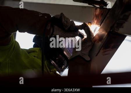 Industrial welding work under steel framework with protective visor and gloves, highlighting metal construction, assembly and skilled trade labor Stock Photo