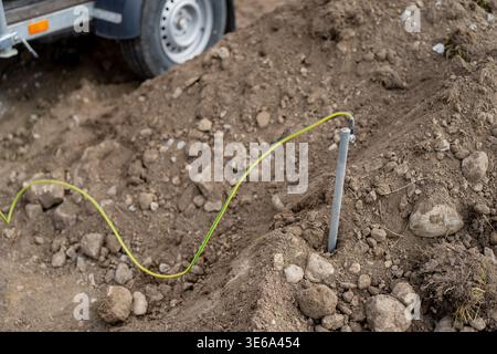 Grounding wire connected to metal rod in excavation soil, showing electrical earthing installation and utility infrastructure work on site Stock Photo
