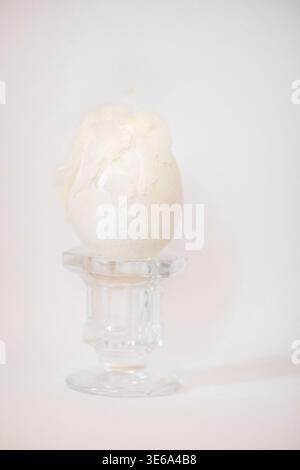 Decorative white egg with intricate shell details placed on a clear glass stand, set against a soft, neutral backdrop suitable for seasonal decoration Stock Photo