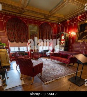 Warwick, UK - 12 Apr 24: Ornate red state room at Warwick Castle with period furniture, patterned carpet, draped curtains and gilded wall panelling. Stock Photo