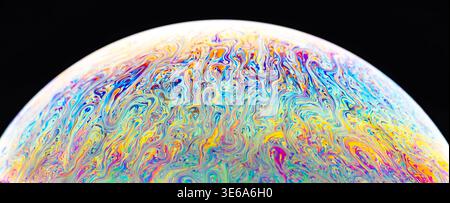 Abstract macro view of a soap bubble's surface displaying vibrant, swirling patterns of light refraction and interference against a dark backdrop Stock Photo