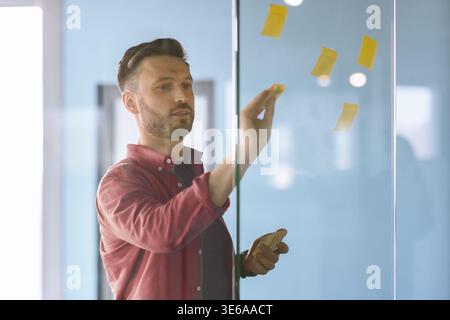 Man Writing on Sticky Notes During a Brainstorming Session in a Modern Office Stock Photo