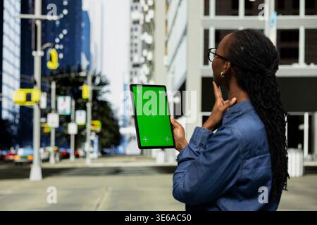 Green screen mockup tablet used by worker walking on city streets, going to work. African american teleworker with chroma key isolated screen touchscreen device in hand doing freelancing outside Stock Photo