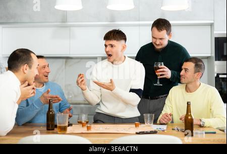 Group of cheerful men engaged in alcohol-fueled board game Stock Photo