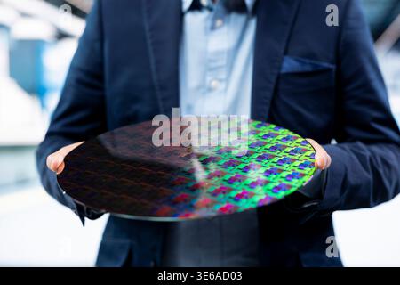 Microchip factory manager looking at microelectronic semiconductor substrate. Expert in business suit analyzing automated machinery silicon wafers production yield in industrial manufacturing plant Stock Photo