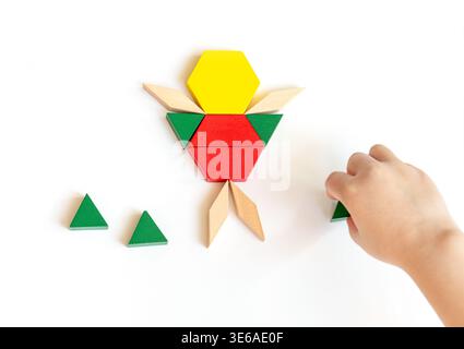 Colorful wooden geometric shapes arranged into a figure with a hand reaching to place additional pieces on a white background Stock Photo