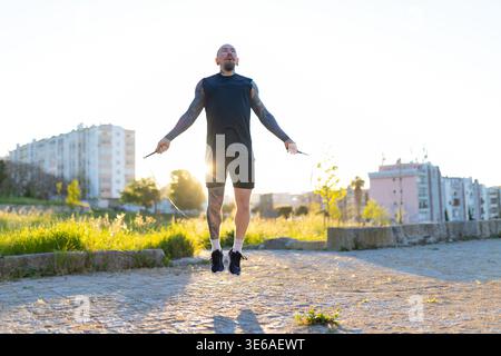 Tattooed man actively performing a skip rope workout in a park Stock Photo