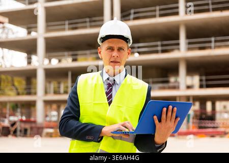 Professional positive man in jacket and helmet working at electonic device outdoor Stock Photo