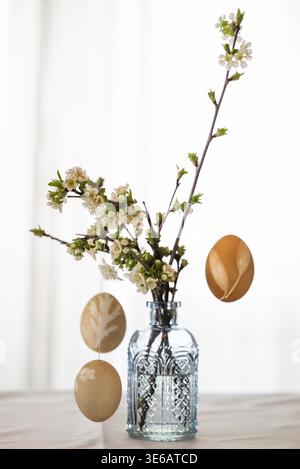 Blown out Easter eggs hang from blossoming branches that stand in a light blue vase against a light background Stock Photo