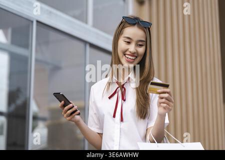 A joyful young woman smiles while holding her smartphone and a credit card, showcasing the excitement of online shopping and digital transactions Stock Photo