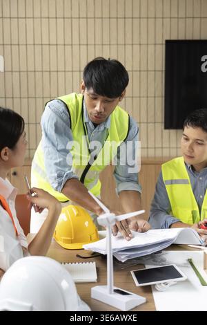 An engineer engages with colleagues, discussing project plans and sustainability strategies in a modern office, emphasizing teamwork and innovative so Stock Photo