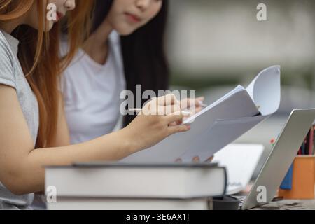 Close-up of two diverse university students studying outdoors, taking notes on papers while collaborating next to a laptop Stock Photo