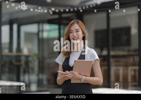 Beautiful Asian women Barista smiling and using tablet at her cafe Stock Photo