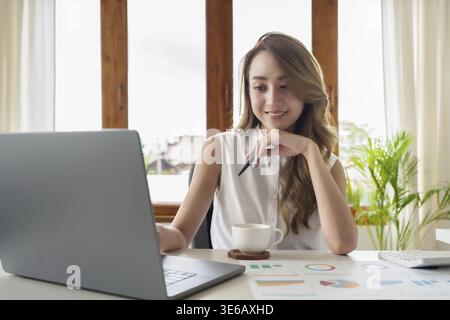 Attractive smiling young asian woman on a video call by laptop computer Stock Photo