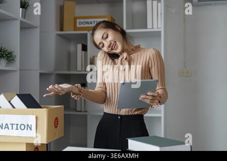 A woman coordinating online donations using a tablet while on the phone, engaged in her role at a charity organization Stock Photo