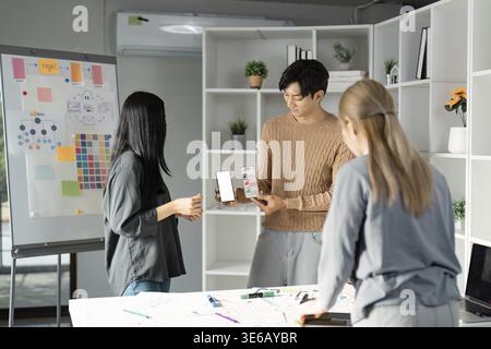 Designers showcasing a mobile app mockup during a UX UI presentation, emphasizing teamwork and interactive design processes in a creative workspace Stock Photo