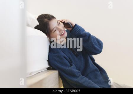 Portrait of Young Asian woman talking with her friend by smartphone sitting on floor at bedroom. Lifestyle concept Stock Photo