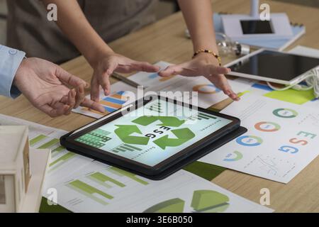 Team members engage in a collaborative discussion about ESG data, analyzing sustainability metrics on a tablet during a meeting Stock Photo