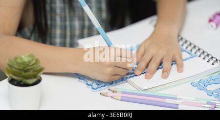A young student engages in creative writing, showcasing the excitement of back-to-school with colorful stationery and a bright notebook Stock Photo