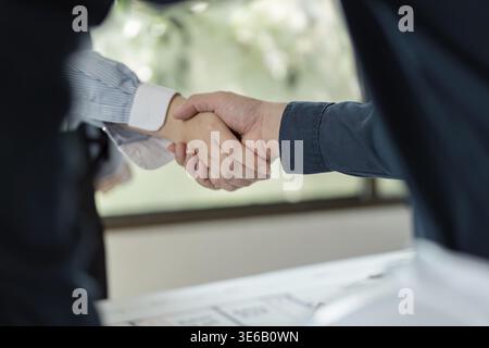 Two engineers shaking hands to confirm their collaboration on an architectural project in a professional office environment Stock Photo