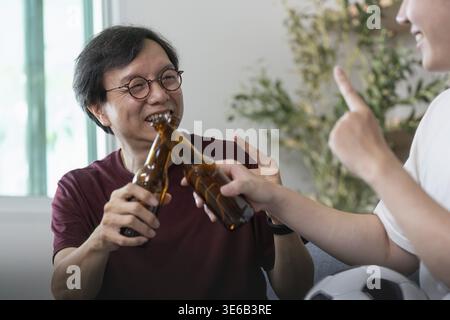 Two friends enjoying a casual moment, clinking beer bottles while sharing laughter and joy over a soccer game Stock Photo