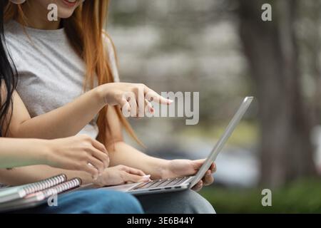 Close-up of two students pointing at a laptop screen, showcasing their collaboration and enthusiasm for learning in a lively outdoor environment Stock Photo