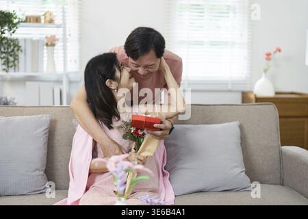 Elderly couple enjoying Valentine's Day, exchanging gifts and affection in a warm, inviting home environment Stock Photo