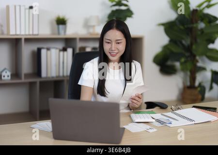 A young woman joyfully organizes her financial documents at her home office, emphasizing remote work efficiency and comfort Stock Photo