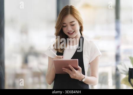 Beautiful Asian women Barista smiling and using tablet at her cafe Stock Photo