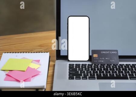Mock up smartphone device with blank screen standing on laptop computer with credit card. Online shopping concept Stock Photo