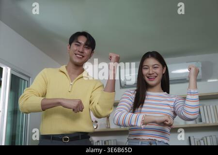 A young couple having fun and dancing together during a video call, highlighting connection and joy in a modern home Stock Photo