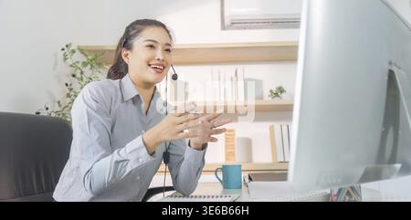 A cheerful woman engages in a virtual meeting, showcasing effective communication skills and professionalism in her home office Stock Photo