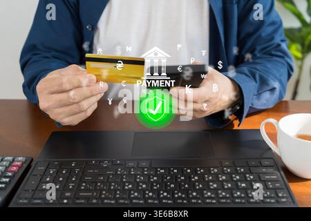 Close-up of hands holding a smartphone and credit card above a laptop with secure payment and currency overlay icons, ideal for fintech, online bankin Stock Photo