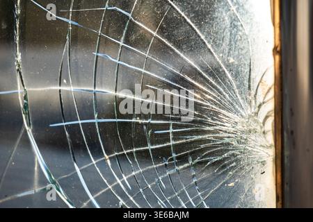 Close-up spiderweb fracture pattern of cracked tempered glass backlit by warm sunlight Stock Photo