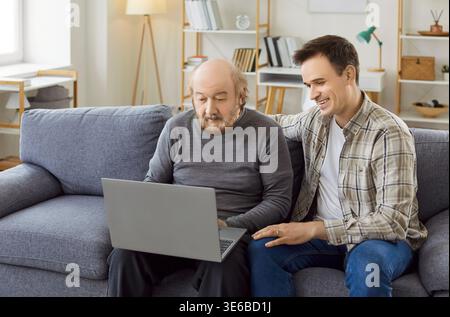 Young man helping adult son teaching interested mature senior father using laptop computer Stock Photo