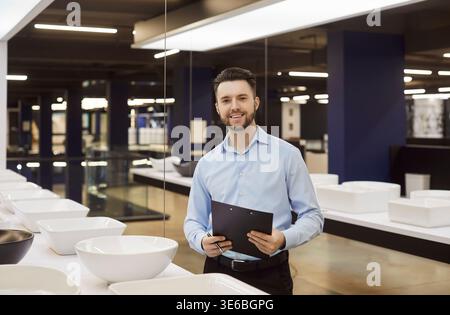 Portrait of happy smiling young salesman standing in plumbing shop and looking cheerful at camera. Stock Photo