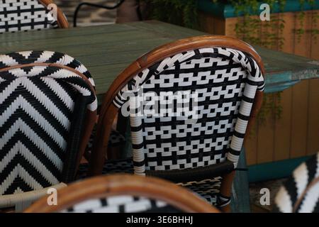 Close-up of patterned woven chairs around table in outdoor café patio setting. Stock Photo