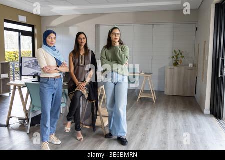 Diverse female coworkers standing together discussing project in bright modern office with monitor Stock Photo