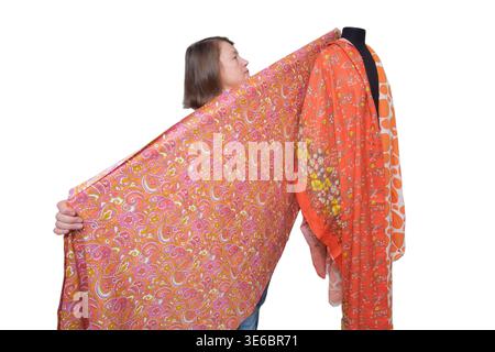 Woman tailor displaying floral fabric on mannequin. Professional fashion designer working with orange textile. Patterned scarf presentation. Creative Stock Photo