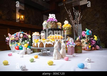 Festive Easter dessert table with colorful cakes, eggs, and floral decorations on stone wall Stock Photo