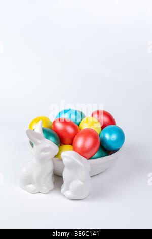 White Porcelain Bunnies and Painted Easter Eggs in Ceramic Bowl on White Background Stock Photo