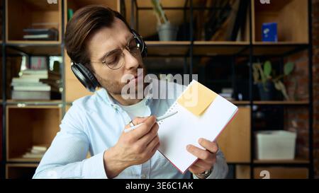 Man with headphones showing notes in notebook with sticky note in office. Stock Photo
