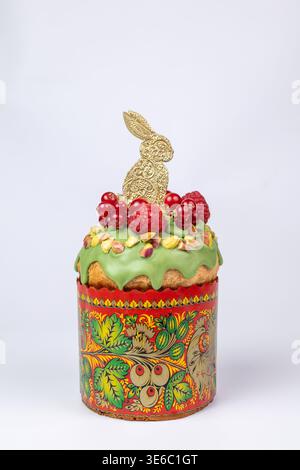 Easter Kulich in Decorated Paper Mold with Green Icing, Raspberries, Pistachios, and Golden Bunny Stock Photo