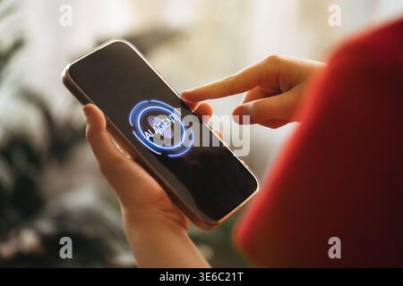 Individual interacts with smartphone featuring AI interface on screen, hand touching display, with blurred indoor plants and soft lighting in the back Stock Photo