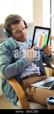 Man with headphones showing growth chart on tablet during online coaching. Stock Photo
