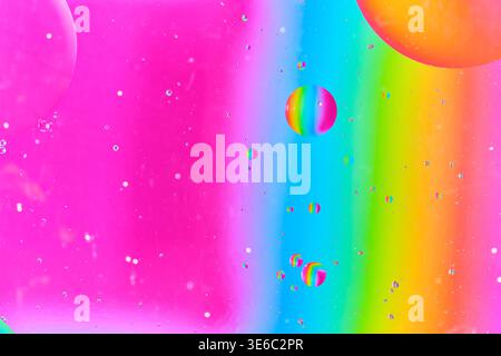 Multicolored oil bubbles suspended in bright spectrum pink, blue, and yellow liquid hues Stock Photo